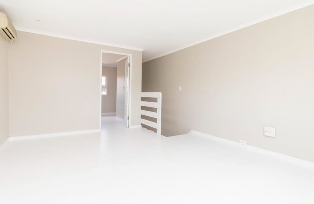 Bright upstairs room with fresh paint, white floor, and stair landing